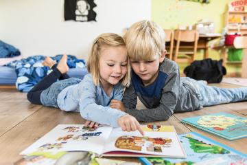 Zwei Geschwister, ein Mädchen und ein Junge, liegen am 26. September 2016 auf dem Boden im Wohnzimmer in Bonn und lesen gemeinsam in einem Kinderbuch. Die Schwester zeigt ihrem Bruder mit dem Finger ein Bild in dem Bilderbuch. (Modelrelease vorhanden)