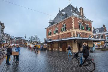 Radfahrer fahren am 11. Dezember 2017 in Leeuwarden über das Kopfsteinpflaster auf der Nieuwstad Straße, vorbei am Waag, einem Nationaldenkmal. Leeuwarden in Friesland ist Europäische Kulturhauptstadt 2018.