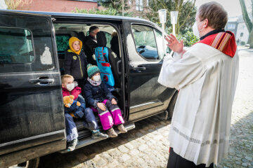 Pfarrer Markus Thoms hält zwei gekreuzte Kerzen und spendet vor dem Auto einer Familie den Blasiussegen im "Drive-in" am 31. Januar 2021 in Neuenkirchen.