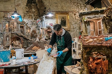 Ein Mann steht in seiner Werkstatt und arbeitet an einer Krippe am 19. November 2021 in der Via San Gregorio Armeno in Neapel. Um ihn herum stehen weitere Krippen, an der Wand hängt ein Heiligenbild.