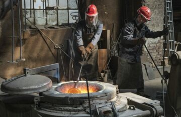 Arbeiter mit Helm und Gesichtsschutz arbeiten an einem glühenden Schmelzofen bei der Produktion einer Glocke am 22. April 2022 in der Werkstatt der Glocken- und Kunstgießerei Rincker in Sinn.