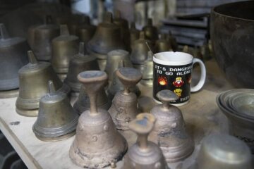 Kleine Glocken auf einem Regalboden, daneben eine Kaffeetasse, am 22. April 2022 in der Werkstatt der Glocken- und Kunstgießerei Rincker in Sinn.