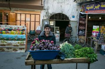 Ein Junge steht in Gaza auf dem Marktplatz hinter einem Stapel verschiedener Gemüsesorten.