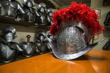 Ein neuer Helm mit traditionellem roten Federschmuck liegt auf einem Tisch in der Waffenkammer der Päpstlichen Schweizergarde im Vatikan am 27. April 2018. Dahinter sind im Regal Rüstungen und Helme aufgereiht.