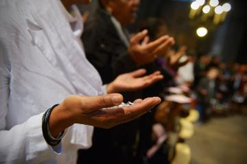 Menschen halten die Hände mit den Handflächen nach oben, während sie das Vaterunser beten, am 11. November 2014 in der Kirche Saint-Sulpice in Paris. Eine Frau hält einen Rosenkranz in der Hand.