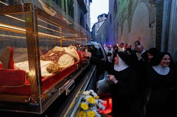 Eine Ordensfrau berührt den gläsernen Sarg mit dem Leichnam des heiligen Papstes Johannes XXIII. am 24. Mai 2018 auf der Ladefläche eines Pick-ups während einer Prozession durch Bergamo.
