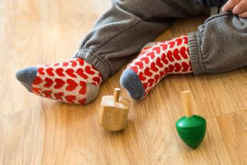 Blick auf die Füße eines Kleinkindes neben zwei Dreideln, Kreiseln, aus Holz am 15. Dezember 2016 in einem Haus in Nataf (Israel). Das Kind trägt Söckchen mit roten Herzen.