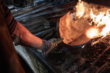 Eine Hand hält ein Metallteil in ein loderndes Feuer am 18. April 2018 in einer Schmiede in Molln (Österreich).