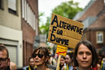 Eine Demonstrantin mit Sonnenbrille hält am 12. Mai 2018 auf dem 101. Katholikentag in Münster auf einer Protestveranstaltung gegen die AfD (die Partei Alternative für Deutschland) ein Schild hoch mit der Aufschrift "Alternative für Dumme". Darunter ist ein kleineres Schild angebracht mit den Worten "Menschenwürde" und (durchgestrichen) "Fremdenhass".