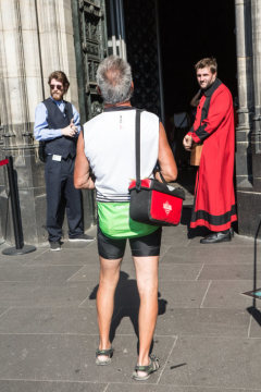 Ein Domschweizer kontrolliert am 2. August 2018 Touristen am Haupteingang des Kölner Doms. Ein Mann in kurzer Radlerhose läuft auf den Eingang zu.