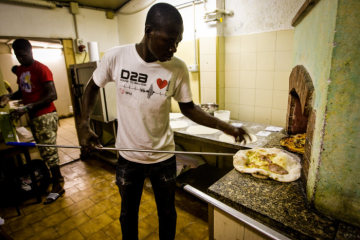 Ein Flüchtling am Steinofen in Pistoia am 25. August 2018. Er arbeitet für die Initiative "Pizzeria dal rifugiato" (dt. Pizzeria beim Flüchtling). Flüchtlinge, die über die lokale katholische Kirche untergebracht sind, backen jeden Samstagabend Pizza und bieten sie gegen Spenden an.