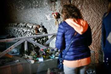 Eine Frau im Gebet vor aufgestapelten Schädeln im Höhlensystem des Friedhofs Fontanelle an Allerheiligen, dem 1. November 2016 in Neapel.