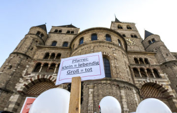 Plakat mit der Aufschrift "Pfarrei: Klein = lebendig - Groß = tot" bei der Protestaktion "5 vor 12" gegen Großpfarreien der Initiative "Kirche vor Ort" am 20. Oktober 2018 vor dem Dom in Trier.