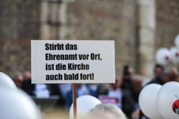 Plakat mit der Aufschrift "Stirbt das Ehrenamt vor Ort, ist die Kirche auch bald fort!" bei der Protestaktion "5 vor 12" gegen Großpfarreien der Initiative "Kirche vor Ort" am 20. Oktober 2018 in Trier.
