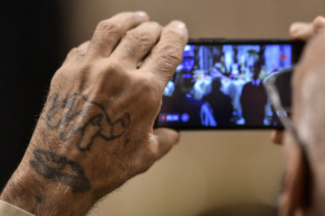 Ein Gottesdienstteilnehmer mit Tätowierung auf der Hand macht ein Foto mit dem Smartphone bei der Papstmesse im Petersdom zum katholischen "Welttag der Armen" am 18. November 2018 im Vatikan.