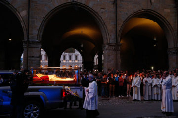 Der gläserne Sarg mit dem Leichnam des heiligen Papstes Johannes XXIII. am 24. Mai 2018 auf der Ladefläche eines Pick-ups vor der Kathedrale von Bergamo. Priester stehen hinter dem Sarg.