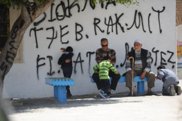 Ältere Männer sitzen im Schatten eines Baumes in Kairouan (Tunesien) am 22. April 2017. Kinder spielen Verstecken.