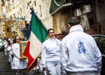 Eine junge Frau steht mit einer italienischen Flagge an der Spitze einer Prozession während der Wallfahrt zur Madonna dell'Arco zu Ostern am 1. April 2018 in Sant'Anastasia (Neapel). Hinter ihr laufen weiß gekleidete Kinder mit Bannern.