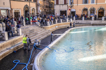 Ein umgebauter Poolsauger saugt am 15. März 2019 Münzen vom Grund des Trevibrunnens in Rom. Daneben schieben Männer die Münzen in die Mitte des Brunnens. Touristen schauen dabei zu.