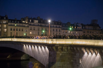 Menschen stehen dicht gedrängt auf einer Brücke über der Seine und blicken auf den Brand der Kathedrale Notre-Dame in Paris am 15. April 2019.