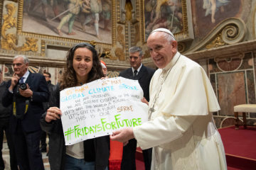 Papst Franziskus empfängt Sinti und Roma am 9. Mai 2019 im Vatikan. Ein Mädchen und er halten ein kleines Plakat zum Thema Klima in den Händen.