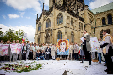 Frauen halten Plakate, darunter eines, das die Muttergottes mit zugeklebtem Mund zeigt, bei einer Mahnwache der Initiative "Maria 2.0" am 12. Mai 2019 vor dem Dom in Münster.