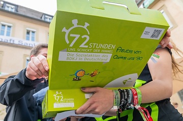 Jugendliche öffnen ein grünes Projekt-Paket mit der Aufschrift "72 Stunden - uns schickt der Himmel. Die Sozialaktion des BDKJ in Deutschland" während der Auftaktveranstaltung zur 72-Stunden-Aktion des BDKJ (Bund der Deutschen Katholischen Jugend) am 23. Mai 2019 in Würzburg.