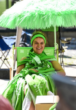 Bei der Eröffnung des Deutschen Evangelischen Kirchentags (DEKT) am 19. Juni 2019 in Dortmund sitzt eine junge Frau, bekleidet mit grünen Kirchentagsschals, in einem grünen Regiestuhl unter einem grünen Sonnenschirm.