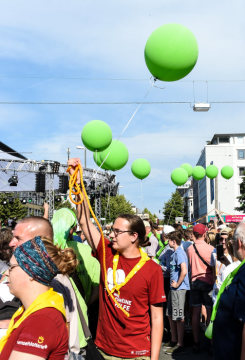 Ein Helfer mit rotem T-Shirt und gelbem Halstuch und andere Menschen halten grüne Luftballons bei der Eröffnung des Deutschen Evangelischen Kirchentags (DEKT) am 19. Juni 2019 in Dortmund.