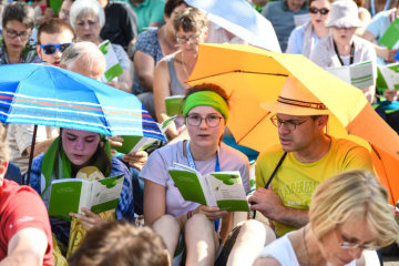 Menschen halten offene Programmhefte und schützen sich mit Regenschirmen vor der Sonne bei der Eröffnung des Deutschen Evangelischen Kirchentags (DEKT) am 19. Juni 2019 in Dortmund.