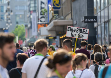 Menschen gehen dicht gedrängt am 22. Juni 2019 auf dem Deutschen Evangelischen Kirchentag (DEKT) in Dortmund. Auf einem Schild steht "Eine Bibel für Sie".