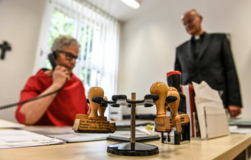 Stempel mit der Aufschrift "Bischof von Essen" stehen am 2. September 2019 im Bischofshaus in Essen auf einem Schreibtisch, während Franz-Josef Overbeck, Bischof von Essen, mit seiner Assistentin spricht.