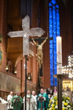 Ein Kreuz und eine Kerze mit dem Logo des Synodalen Wegs beim Gottesdienst zur Eröffnung der Synodalversammlung am 30. Januar 2020 im Frankfurter Dom Sankt Bartholomäus, dahinter unscharf Bischöfe.