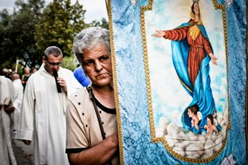 Eine Frau trägt in einer Prozession eine Fahne mit dem Abbild Mariens zu Mariä Himmelfahrt in Licusati (Italien) am Abend des 14. August 2015. Hinter ihr geht ein Geistlicher.