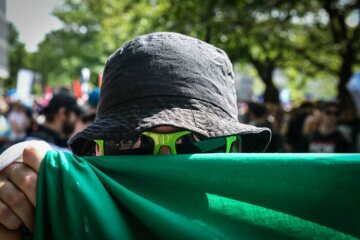 Ein Demonstrant verdeckt sein Gesicht mit Hilfe eines grünen Banners und trägt außerdem einen Hut und eine Sonnenbrille am 12. Mai 2018 in Münster auf einer Protestveranstaltung gegen die AfD (die Partei Alternative für Deutschland).