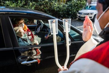 Ein Pfarrer mit Mund-Nasen-Schutz hält zwei gekreuzte Kerzen und spendet den Blasiussegen im "Drive-in" vor der Kirche am 31. Januar 2021 in Neuenkirchen.