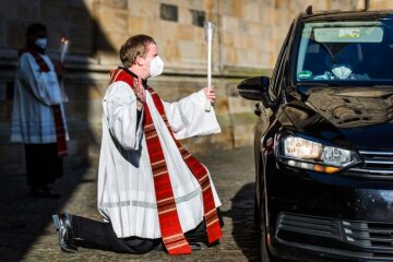 Pfarrer Markus Thoms hält zwei gekreuzte Kerzen und spendet kniend vor einem Auto den Blasiussegen im "Drive-in" vor der Sankt Anna Kirche am 31. Januar 2021 in Neuenkirchen.