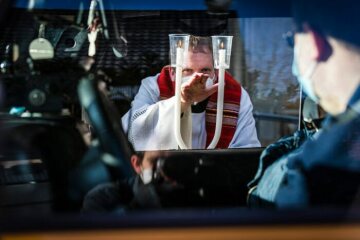 Ein Pfarrer mit Mund-Nasen-Schutz hält zwei gekreuzte Kerzen und spendet den Blasiussegen im "Drive-in" vor der Sankt Anna Kirche am 31. Januar 2021 in Neuenkirchen.