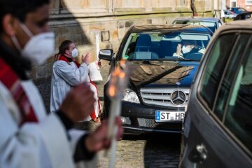 Priester mit Mund-Nasen-Schutz halten zwei gekreuzte Kerzen und spenden vor Autos den Blasiussegen im "Drive-in" vor der Sankt Anna Kirche am 31. Januar 2021 in Neuenkirchen.