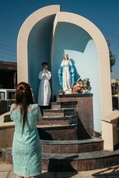 Eine Frau fotografiert einen Jungen in weißer Albe neben einer Statue der Muttergottes, einer Nachbildung der Lourdes-Grotte, nach der Danksagungsmesse zu dessen Erstkommunion in Karakosch (Irak) am 1. Juli 2018.