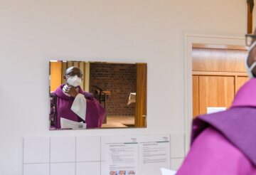 Ein Priester trägt Mundschutz und kontrolliert das Messgewand im Spiegel in der Sakristei vor einem Gottesdienst am 17. Februar 2021 in Bonn.