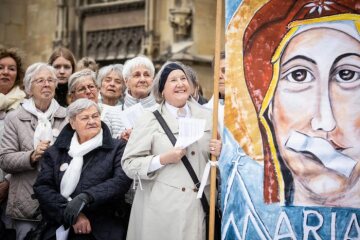 Frauen halten ein Plakat, das die Muttergottes mit zugeklebtem Mund zeigt, bei einer Mahnwache der Initiative "Maria 2.0" am 12. Mai 2019 vor dem Dom in Münster.