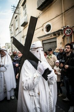 Ein mit weißer Kapuze vermummter Mann mit Dornenkrone trägt ein Holzkreuz bei der Prozession der "Apostoli incappucciati" (dt. Apostel mit Kapuzen) an Gründonnerstag, dem 18. April 2019 auf der Insel Procida (Italien).