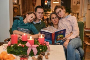 Vater, Mutter und zwei Kinder sitzen am 13. November 2018 in Bonn vor einem Adventskranz und lesen in einem Buch. Drei Kerzen brennen zum 3. Advent.