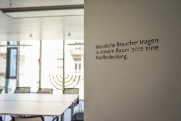 An der Tür zum Beth Midrasch, einem Gebetsraum, in der Hochschule für Jüdische Studien Heidelberg (HfjS) steht der Hinweis "Männliche Besucher tragen in diesem Raum bitte eine Kopfbedeckung.", am 27. Mai 2019. An der Fensterwand im Hintergrund steht ein Chanukkaleuchter.