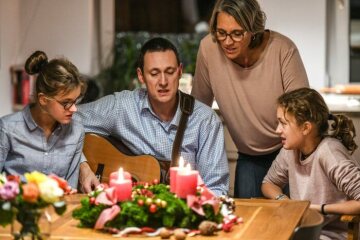 Vater, Mutter und zwei Kinder sitzen am 13. November 2018 in Bonn vor einem Adventskranz und singen. Der Vater spielt Gitarre, am Kranz brennen vier Kerzen zum 4. Advent.