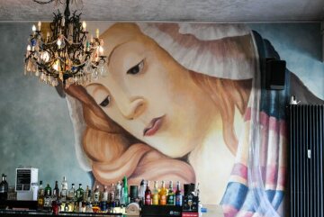 Spirituosenflaschen stehen am 28. Juni 2018 im Kölner Cafe "Maria Eetcafe" hinter dem Tresen. Auf die Wand im Hintergrund ist ein großes Marienbild gemalt. Von der Decke hängt ein Kronleuchter.