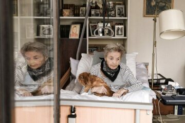 Eine kranke Frau liegt in einem Pflegebett in ihrer Wohnung in Bonn am 8. März 2021 und schaut nachdenklich aus dem Fenster. Sie hält ihre Katze im Schoß.