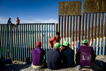 Flüchtlinge aus Südamerika sitzen am 13. November 2018 in Tijuana (Mexiko) vor dem Grenzzaun zur USA. Zwei Männer sitzen auf dem Grenzzaun.