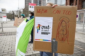 Eine Person hält ein Plakat mit der Aufschrift "We/She can too" (dt. Wir/Sie kann auch), "#outinchurch" und "Für eine Kirche ohne Angst" in den Händen, am 3. Februar 2022 in Frankfurt.
